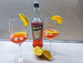 Fľaša s Aperolom a dva poháre s drinkom Aperol Spritz ozdobené pomarančom