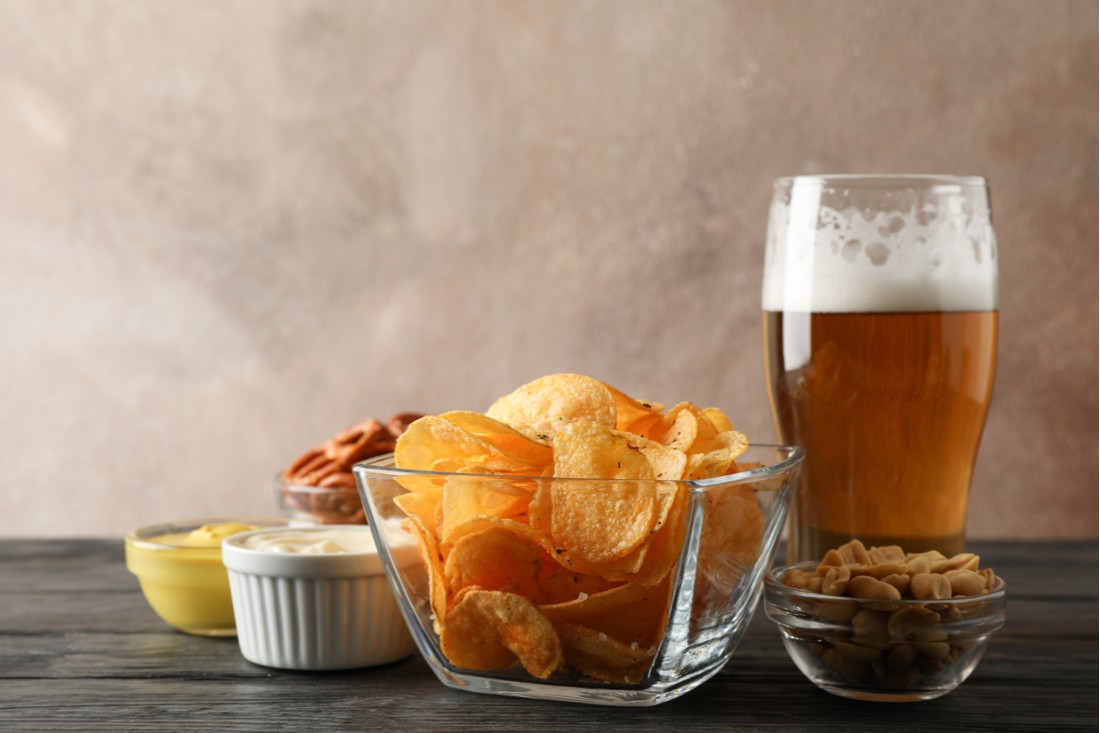 Pivo a kalórie - pohár piva a množstvo nezdravých pochutín v miskách na stole