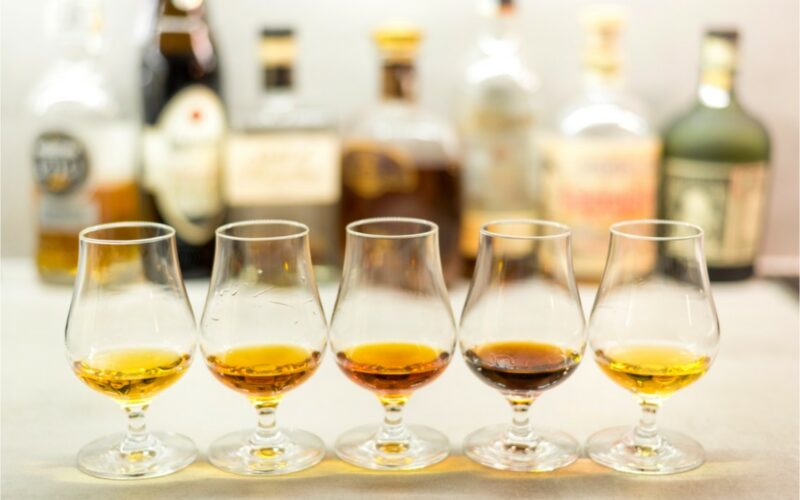 Druhy rumov - degustačné poháriky s rôznymi druhmi rumov, v pozadí fľaše rumu