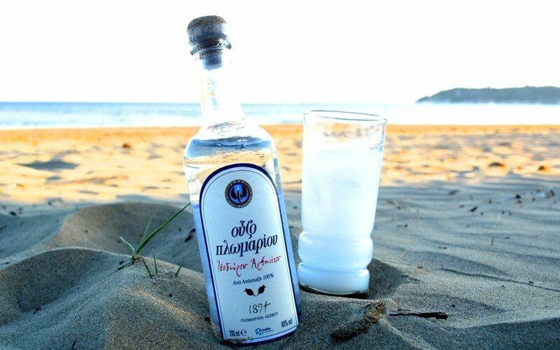 Fľaša Ouzo likéru a pohár na pláži