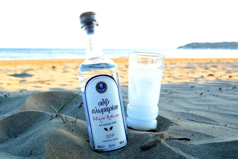 Fľaša Ouzo likéru a pohár na pláži