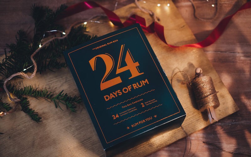 Rumový kalendár 24 Days of Rum - Vianoce a vianočná výzdoba, položený na dreve s vetvičkou