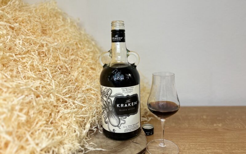 Kraken Black Spiced Rum - fľaša, vrchnák a alkohol v pohári na drevenom podklade