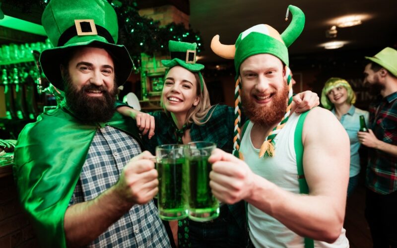 Deň svätého Patrika na zeleno - dvaja muži a žena v typických zelených klobúkoch a s pivom v ruke pri oslave St. Patricks Day