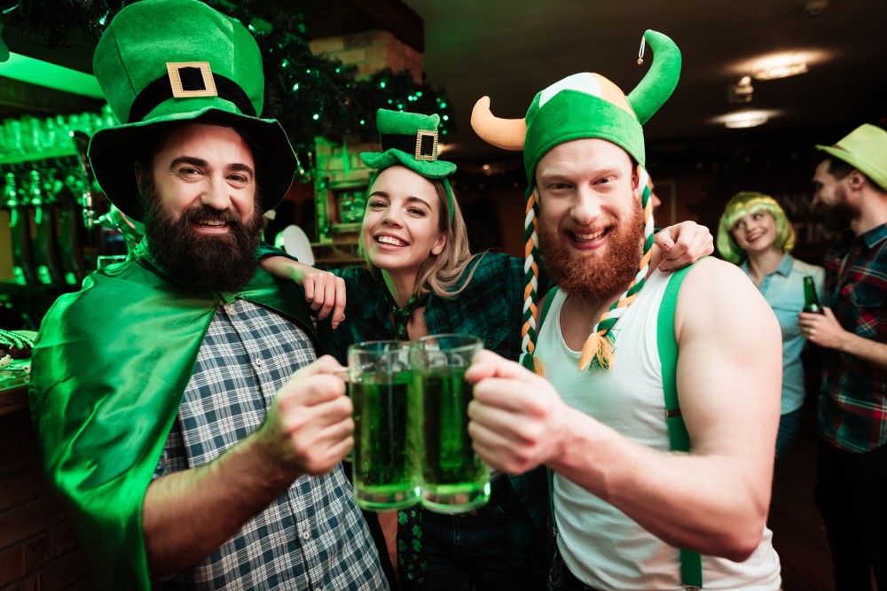 Deň svätého Patrika na zeleno - dvaja muži a žena v typických zelených klobúkoch a s pivom v ruke pri oslave St. Patricks Day