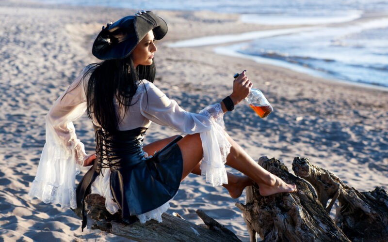 Pirátka s fľašou rumu v ruke na piesočnatej karibskej pláži