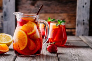 Sangria s pomarančom, jablkom, jahodou a ľadom v džbáne a pohári na rustikálnom drevenom pozadí